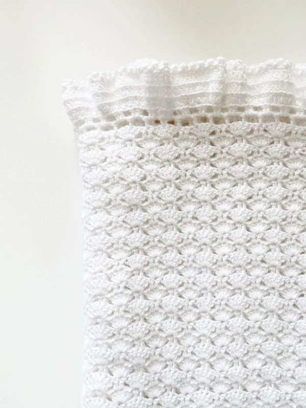 A white shell stitch baby blanket with ruffled edging.