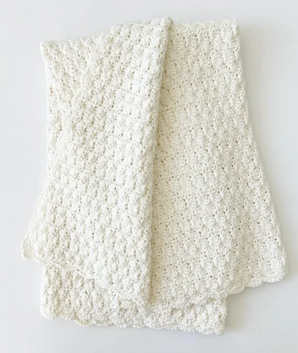 A classic shell stitch baby blanket made in white cotton yarn.
