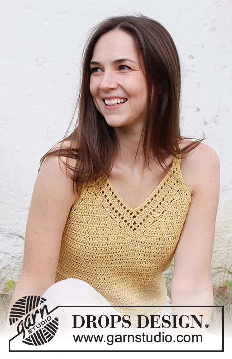 A woman weraing a yellow crochet top with filet crochet detail around the v-neckline.