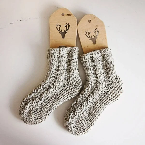 A pair of grey cable-crochet socks on wooden sock forms.