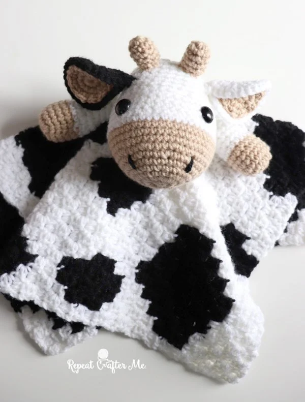 A black and white cow-themed crochet lovey blanket.