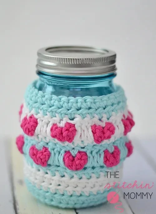 A crochet mason jar cozy with pink hearts.