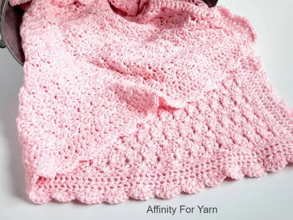 A pink shell stitch crochet baby blanket with a scalloped edge.