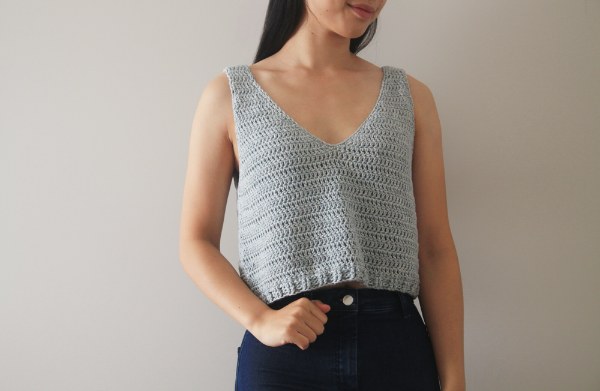 A woman wearing a light grey v-neck crochet tank top.