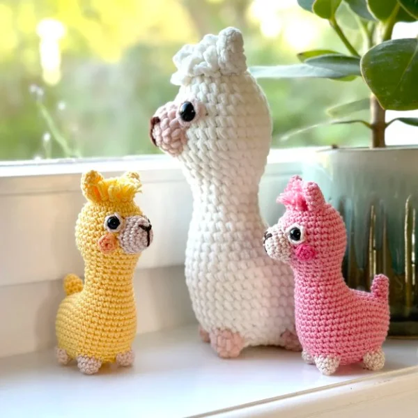 Three colourful crochet alpcas standig on a window sill.