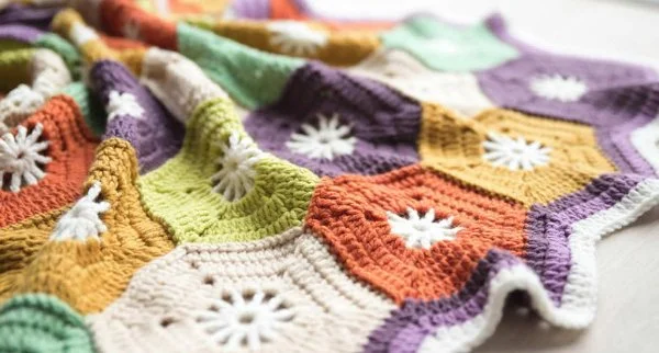 A crochet blanket with brightly coloured hexagons with white centres.