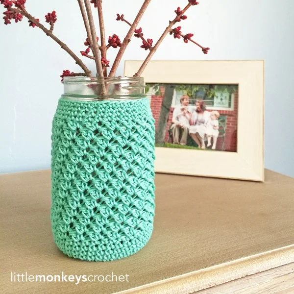 A glass jar/vase with a crochet cover.