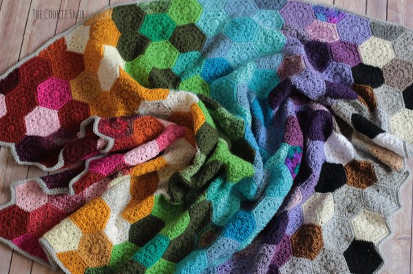 A rainbow coloured crochet blanket made of small solid-coloured hexagons.