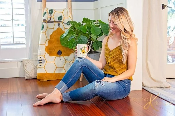 A woman wearing a golden yellow crochet v-neck tank with jeans.