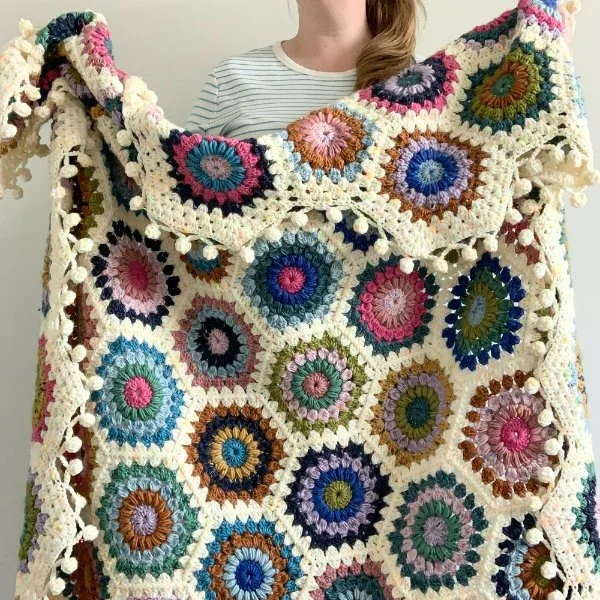 A crochet hexagon blanket with pom-pom style edging.