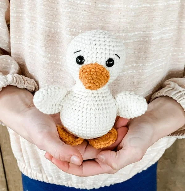 A white crochet duck toy standing in someones hands.