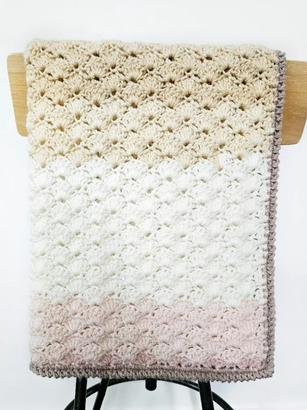 A gradient-yarn, shell stitch baby blanket drraped over a chair. draped