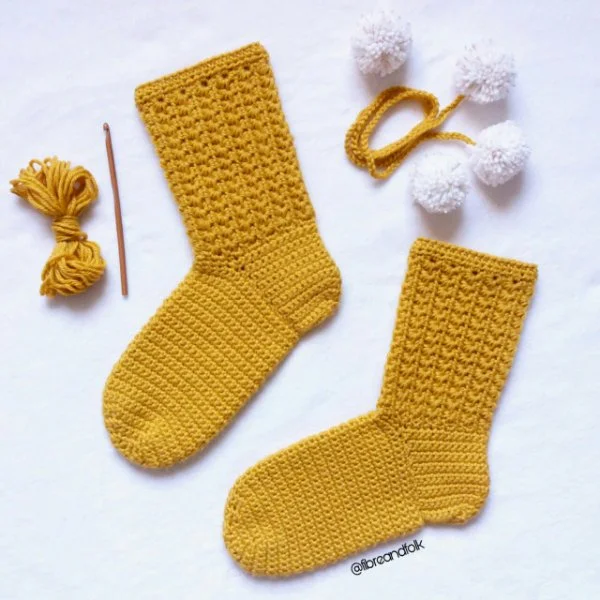 A flat-lay image of crochet materials with a pair of yellow crochet socks featuring the star stitch.