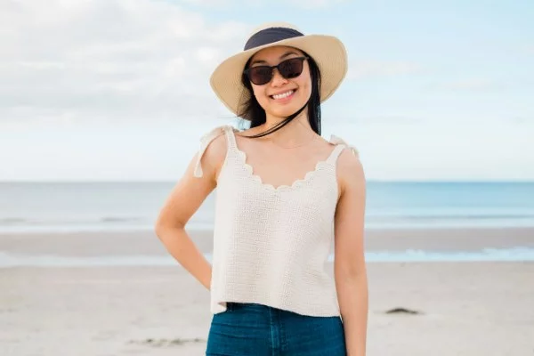 A woman at the beach weraing a v-neck crochet top with scalloped edging.