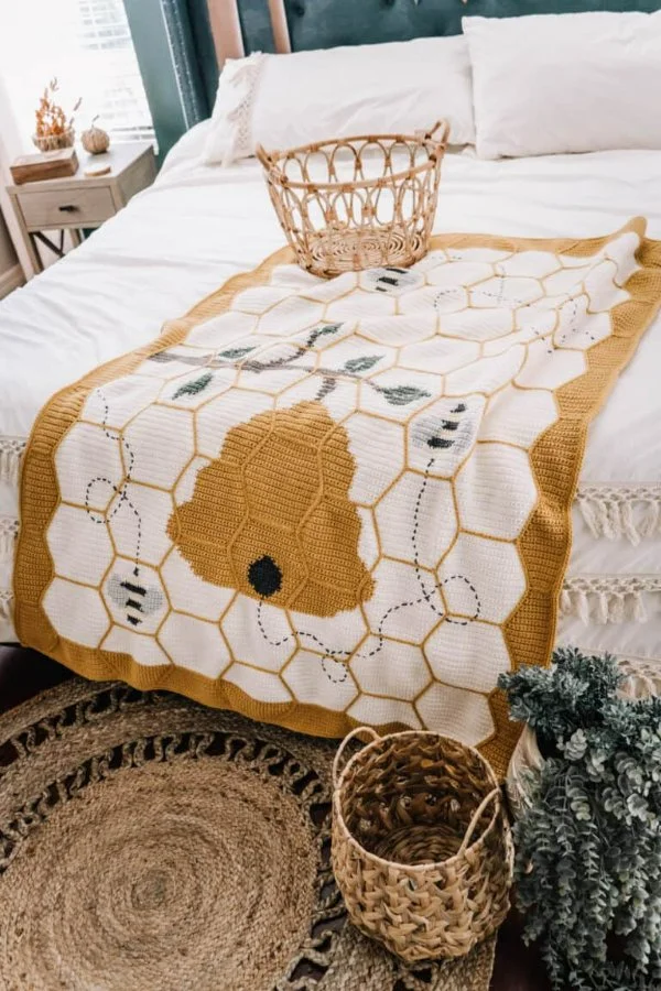 A honey-bee themed crochet hexagon blanket draped across the foot of a bed.