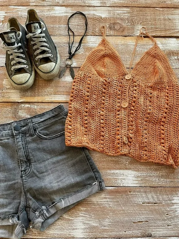A flat lay image of a button-up crochet v-neck tank top, jeans shorts, and converse sneakers.