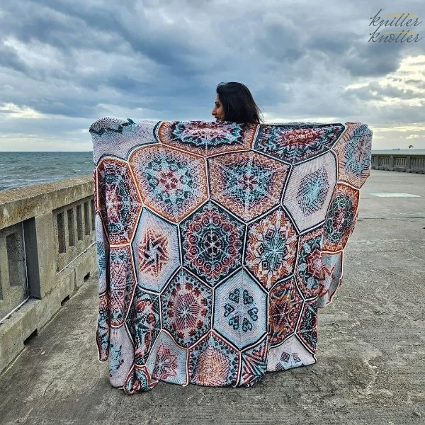 A woman with an intricately detailed Tunisian crochet hexagon blanket draped across her back.