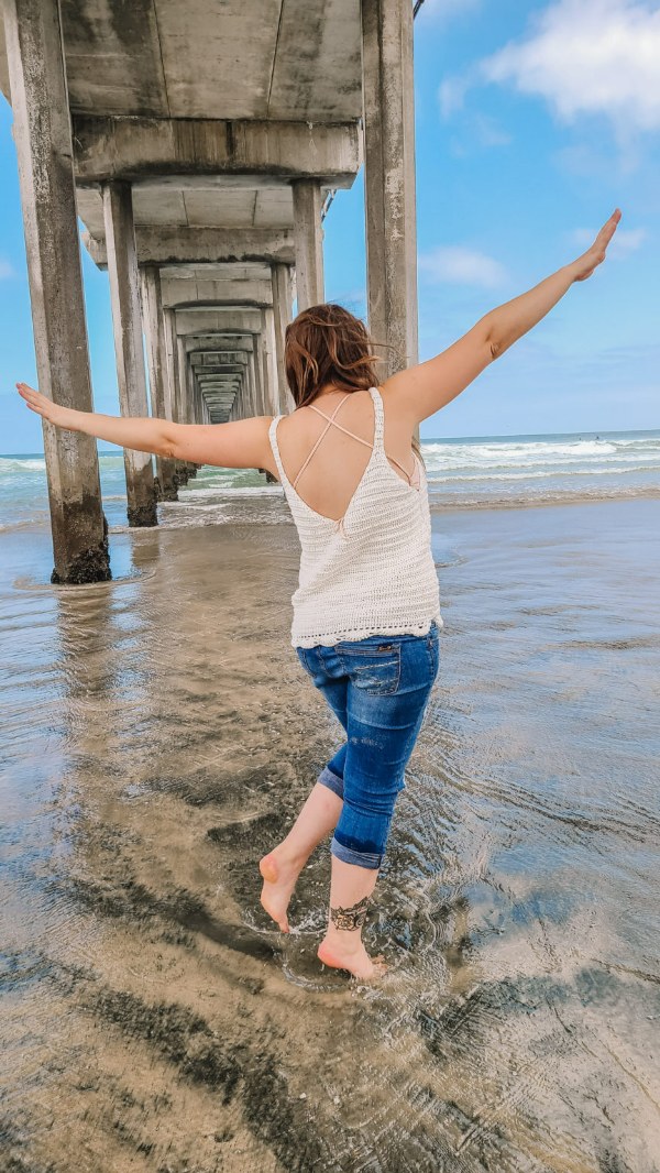 A woman at the beach wering a white crochet v-neck top.