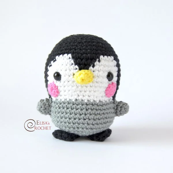 A cartoon-style crochet penguin amigurumi with pink cheeks.