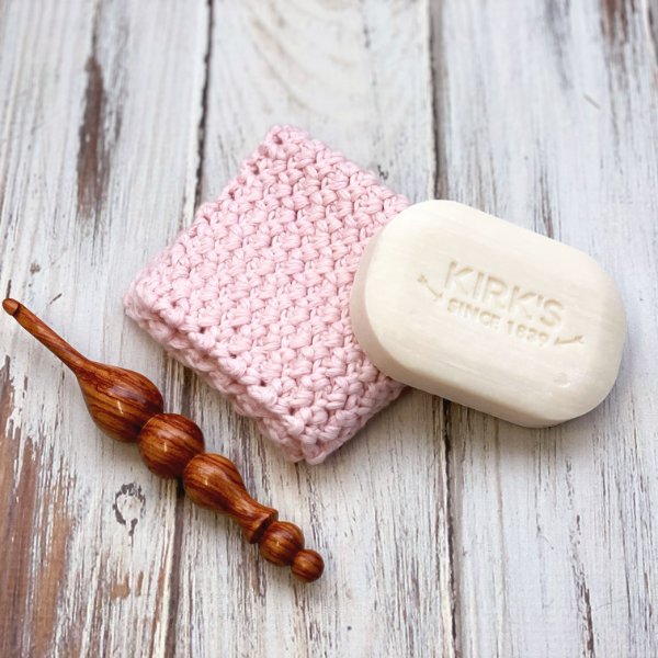 A c2c crochet washcloth, a wooden crochet thook and a bar of soap.