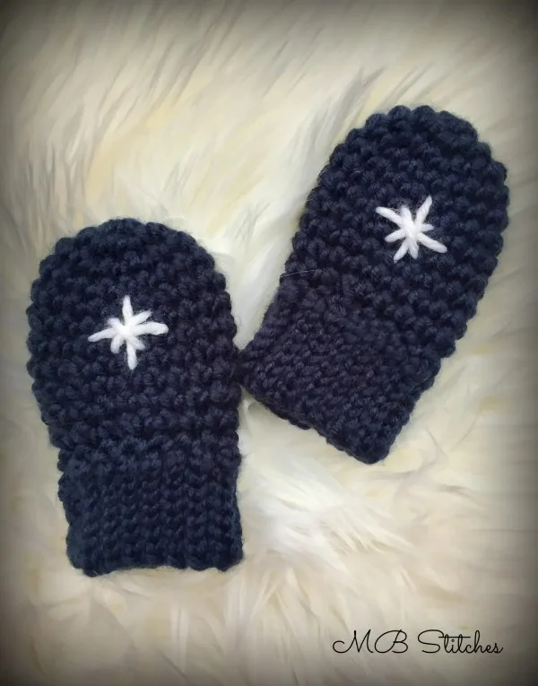 Navy blue crocheted baby mittens with an embroidered snowflake motif.