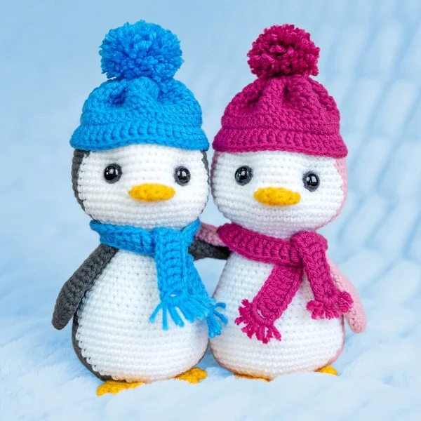 Two crochet penguins standing together wearing brightly coloured beanies and scarves.