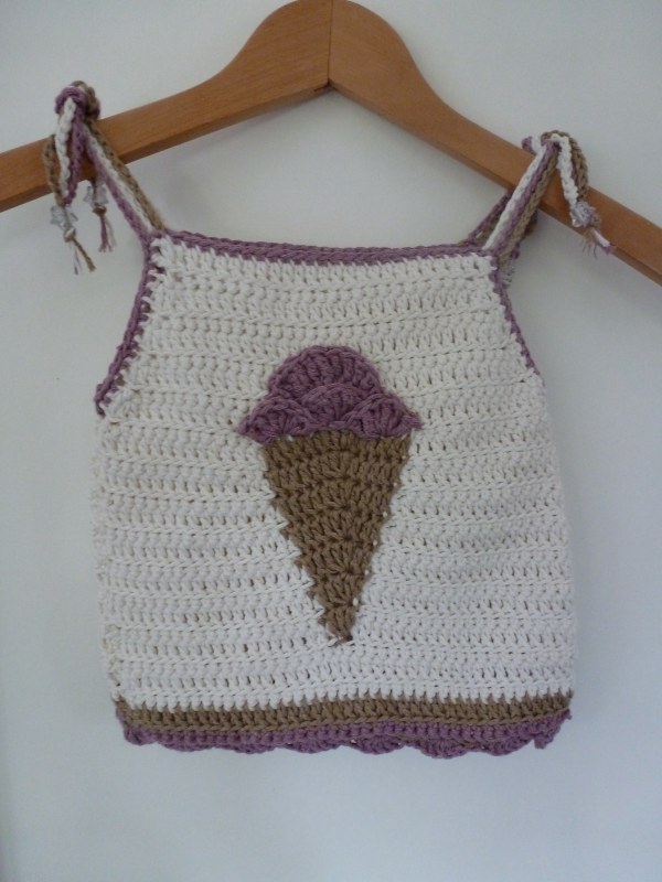 A crochet toddler top with an icecream motif on a wooden hanger.
