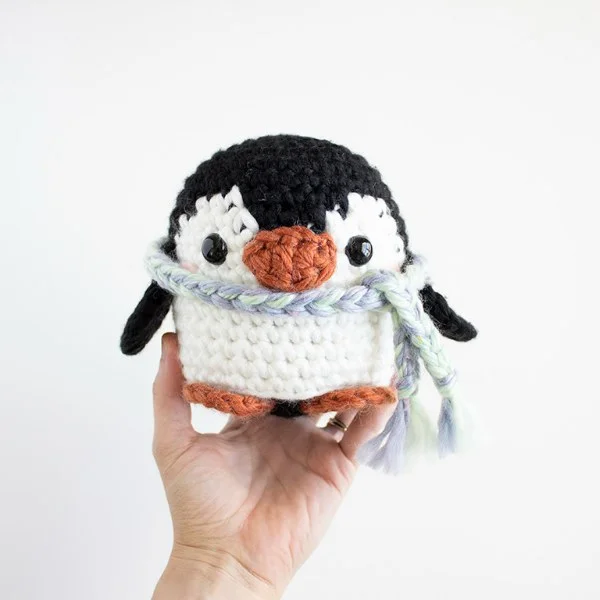 An amirugumi penguin being held in one hand.