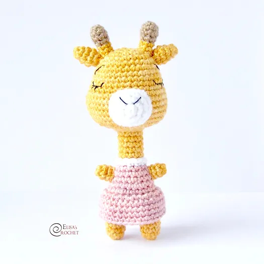 A standing crochet giraffe toy with a long neck and a pink dress.