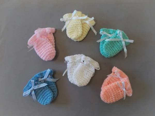 Six pairs of crochet newborn mittens in different colours.