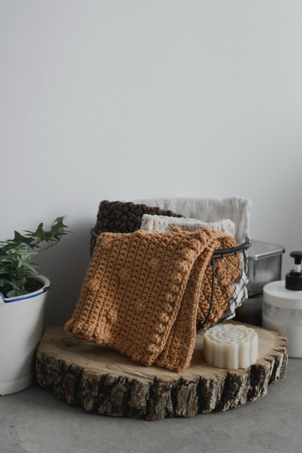 An ochre coloured crochet washcloth featuring the bobble stitch.