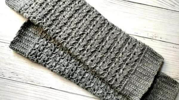 A flat lay image of a pair of grey crocheted leg warmers.