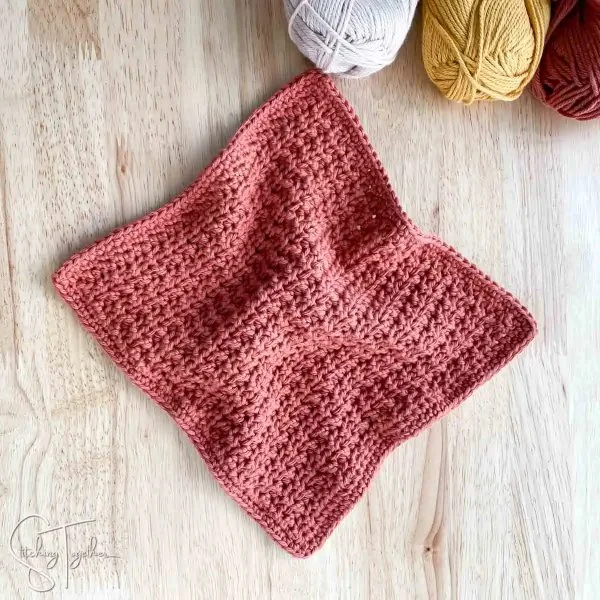 A flat lay image of a rose coloured washcloth on a timber background.