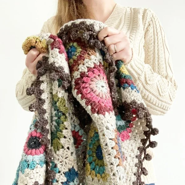 A granny squate blanket with a pompom border.