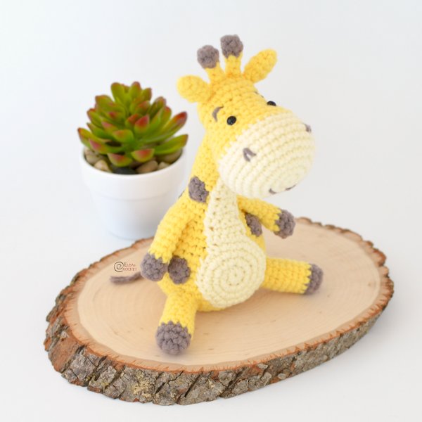 A crochet giraffe sitting on a piece of wood.