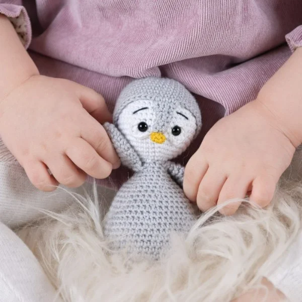 A close up image of a crochet penguin in a babies hands.