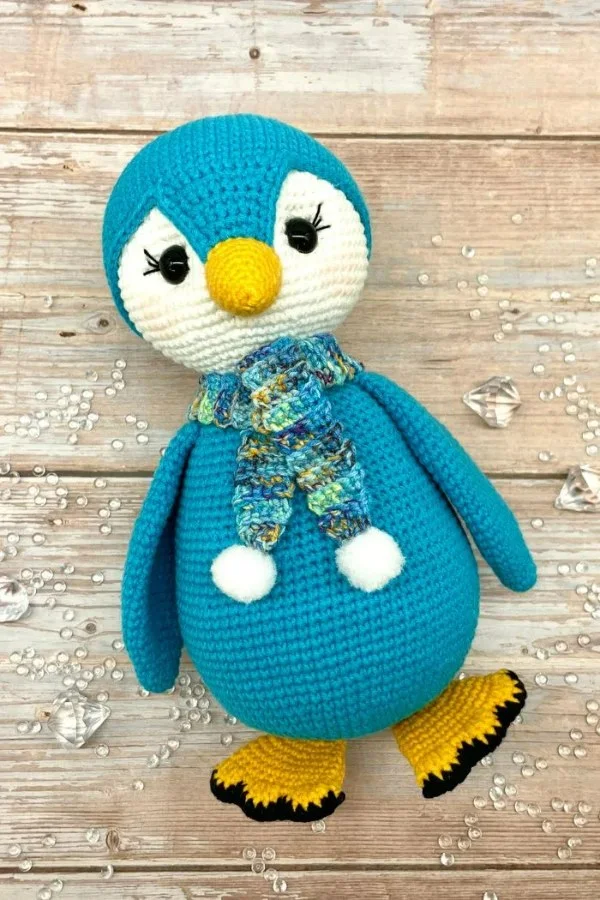 A flat lay image of a blue crochet penguin toy.