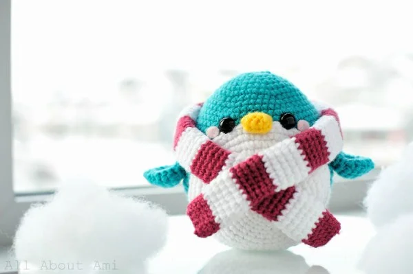 A brightly coloured crochet penguin with a red and white striped scarf.