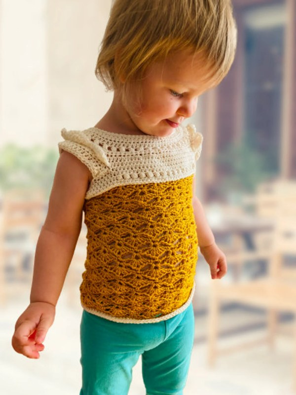 A toddler weraing a yellow and white crochet top with a lacy stitch design.