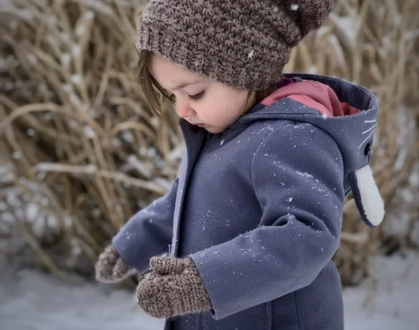 A toddler in the snow wearing brown crochet mittens.