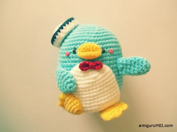 A blue crochet penguin with a bow tie and a hat.