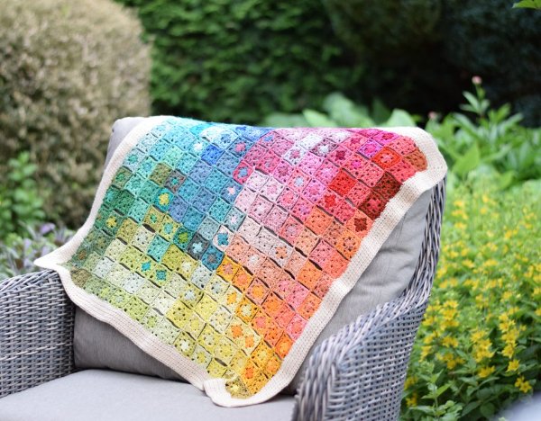 A rainbow coloured granny square blanket in a garden.