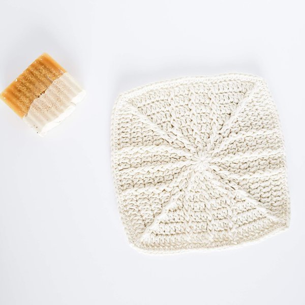 A white crochet washcloth with a windmill vane motif.