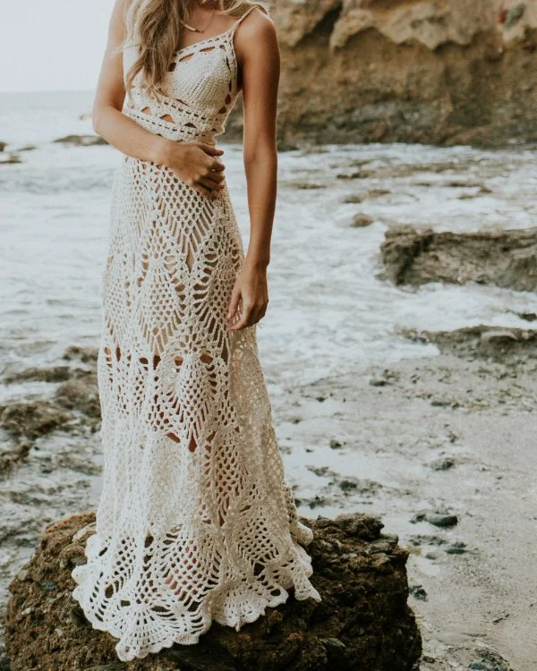A woman at the beach wearing a long lacy crochet skirt and top.