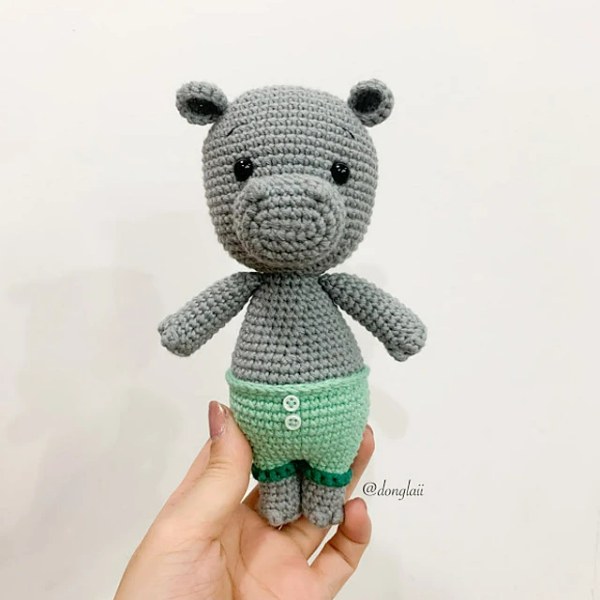 A small baby hippo amigurumi wearing green shorts.