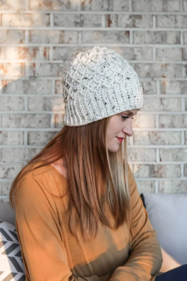 A woman wearing a cable crochet beanie with a diamond pattern.