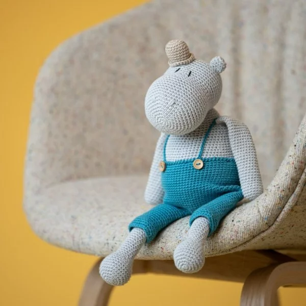 A grey crochet hippo with blue overalls and a bowler hat.