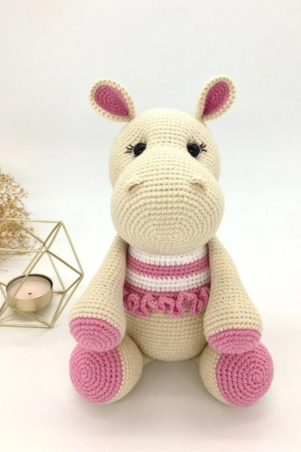 A sitting crochet hippo with a pink and white striped top.