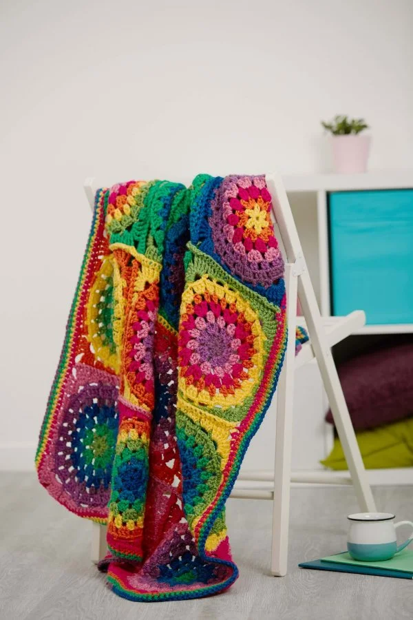 A bright, rainbow-coloured granny square baby blanket.