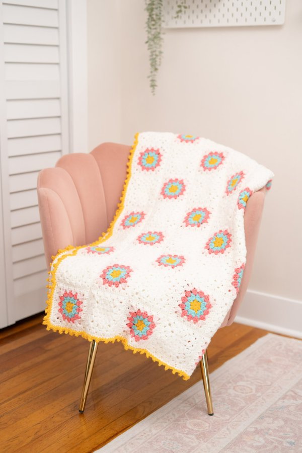 A pastel coloured flower granny square blanket with a yellow border.